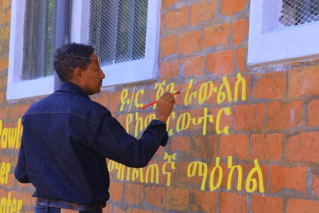 Artisan hand-painting the Amharic title for the Dr. John Rawls Computer Training Center on the exterior brick