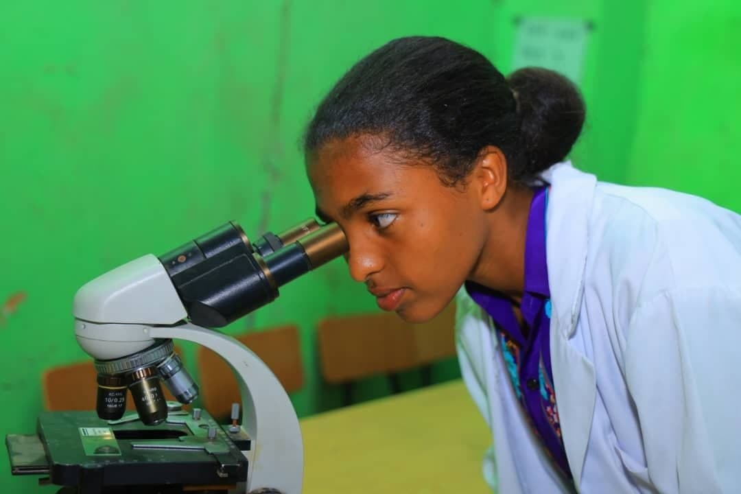 Student in a white laboratory coat conducting practical scientific research with a microscope